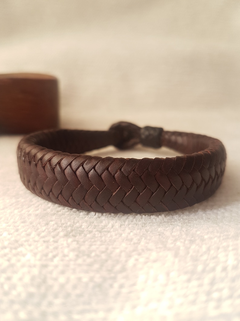 Puede incluir: Un brazalete de cuero marr&oacute;n con un dise&ntilde;o trenzado.