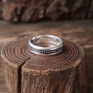 Peut inclure: Une bague en argent avec un motif de perles autour de la bande. La bague est posée sur une surface en bois.