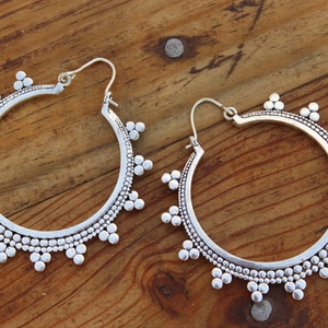 May include: A pair of silver hoop earrings with a beaded design. The earrings are large and have a circular shape.