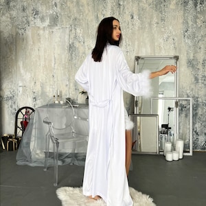 May include: A white satin robe with a long, flowing design and a tie belt. The robe has a faux fur trim around the cuffs and hem.