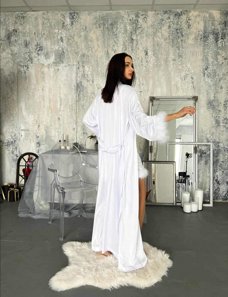 May include: A white satin robe with a long, flowing design and a tie belt. The robe has a faux fur trim around the cuffs and hem.