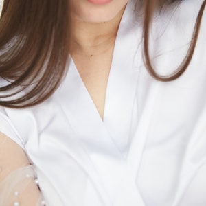 May include: A close-up of a woman's neckline wearing a white button-down shirt with a V-neck. The shirt has a sheer, beaded overlay on the sleeve.