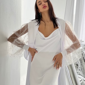 May include: A white dress with a cowl neck and a sheer overlay with pearl embellishments on the sleeves.