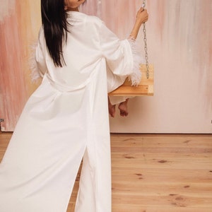 Bridal robe with feather sleeves for bachelorette party. Bride getting ready, long white satin robe with feather