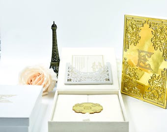 Caja para invitaciones de boda de terciopelo color marfil con invitación de acrílico con espejo dorado y monograma personalizado.