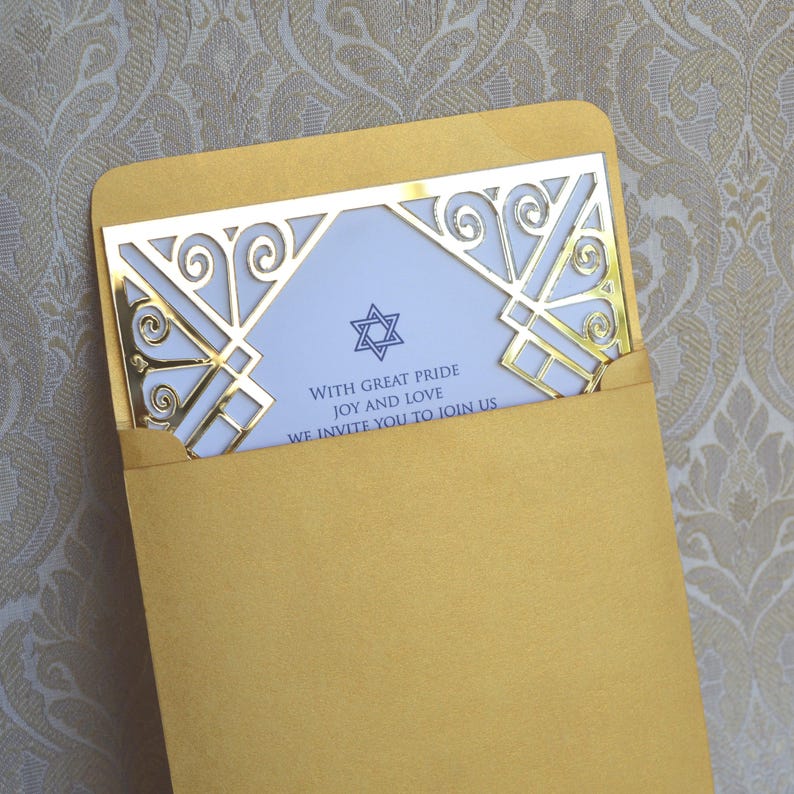 This is a beautiful, elegant Bar Mitzvah invitation featuring a striking gold laser-cut mirror acrylic frame with an intricate Art Deco style. The gold geometric swirls surround a white cardstock center printed with navy blue text and a Star of David at the top.

The combination of the formal serif typography for the details and the flowing script for Jacob's name creates a sophisticated and modern look.