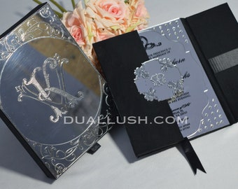 May include: A silver mirror wedding invitation with a black cover and a black ribbon. The invitation features a silver floral design and the text "DUALLUSH.COM".