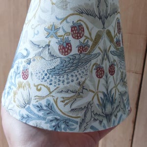 May include: A white lampshade with a blue and green floral pattern featuring birds and strawberries. The pattern is reminiscent of a vintage design.