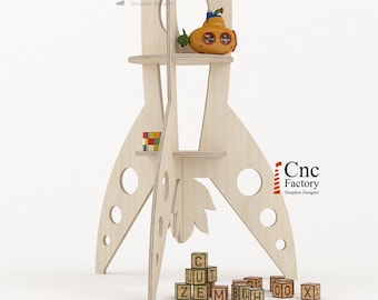 May include: A light-colored wooden rocket-shaped shelf unit with multiple shelves. The shelves hold a yellow frog toy, a yellow submarine toy, and a small block puzzle. Wooden alphabet blocks are at the base.