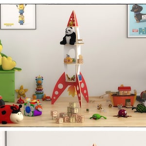 Op de afbeelding: Een rood en wit raketvormig boekenrek met planken voor speelgoed. Het boekenrek heeft een pandabeer knuffel op de bovenste plank en ander speelgoed op de onderste planken. Het boekenrek staat in een kamer met een witte muur en een houten vloer.