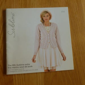Puede incluir: Una portada de libro con una mujer que lleva un cárdigan de punto rosa y una falda blanca. El título del libro es "The fifth Sublime extra fine merino wool dk book" y el subtítulo es "12 designs for women and girls from 2 to adult".