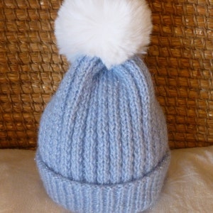 May include: A light blue knitted hat with a white pom-pom on top. The hat has a sparkly finish.