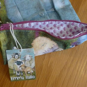 Puede incluir: Un estuche con estampado de ovejas y cremallera morada. El forro interior presenta un patr&oacute;n repetido de peque&ntilde;as ovejas. Una etiqueta con el texto "Emma Ball&reg;" y una ilustraci&oacute;n de ovejas est&aacute; adjunta.