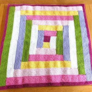 May include: A square, hand-knitted blanket with a log cabin design. The blanket features stripes of white, green, lavender, yellow, and pink, framed by a deep magenta border. The blanket is made of soft yarn and is suitable for a baby or child.