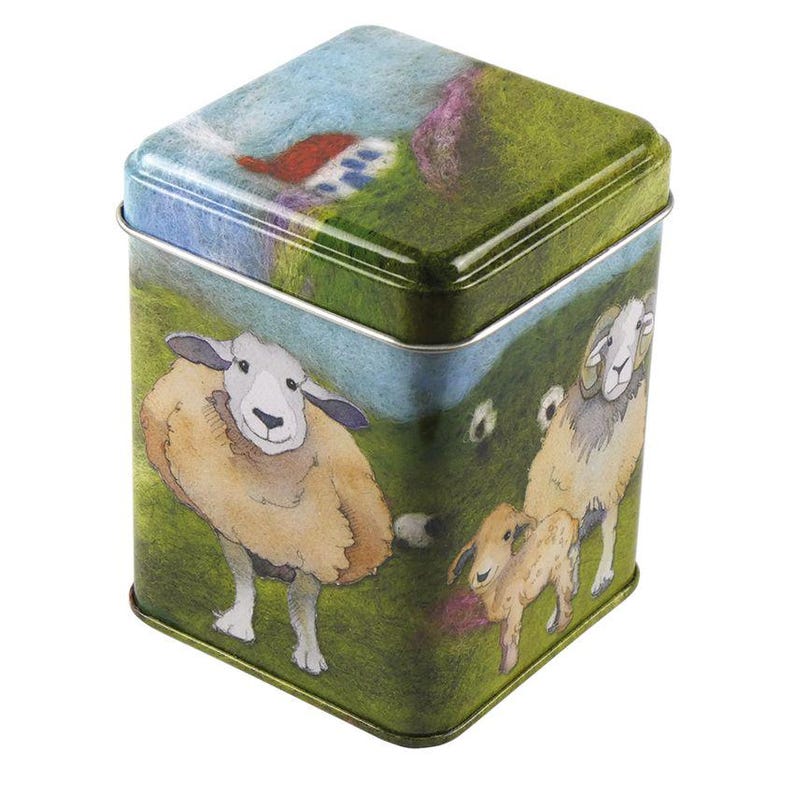 May include: A square green tin with a colorful illustration of sheep on a grassy hillside. The tin has a white rim and a blue sky with white clouds in the background.