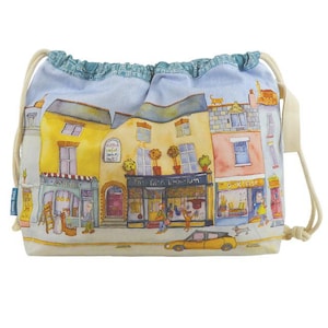 Könnte beinhalten: Ein Kordelzugbeutel mit einer Aquarellillustration einer Stadtstraße. Die Gebäude sind gelb, rosa und blau, mit Geschäften und einem gelben Auto. Der Text "The Yarn Emporium" ist sichtbar. Der Beutel hat einen cremefarbenen Kordelzug.