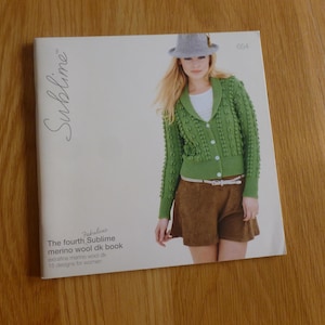Puede incluir: Una portada de libro con una mujer que lleva un cárdigan verde con cuello blanco y pantalones cortos marrones. El título del libro es "Fabulous The fourth Sublime merino wool dk book" y el subtítulo es "extrafine merino wool dk 15 designs for women".