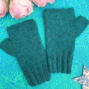 May include: A pair of teal blue fingerless gloves made of a soft, textured knit fabric. The gloves are shown on a patterned background.