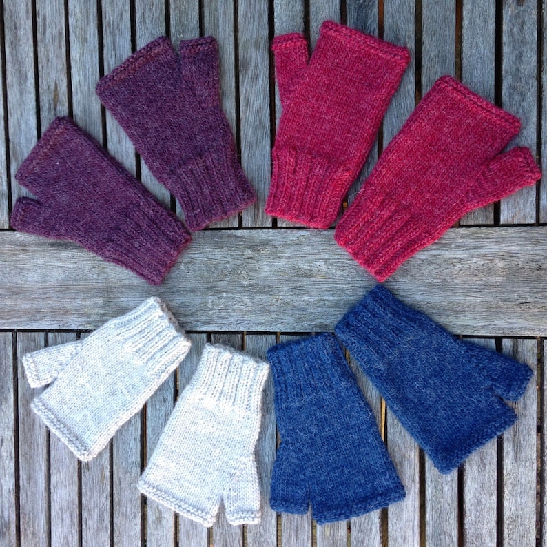 May include: Six pairs of fingerless gloves in various colors, including burgundy, red, beige, and blue. The gloves are laid out in a circle on a wooden surface.