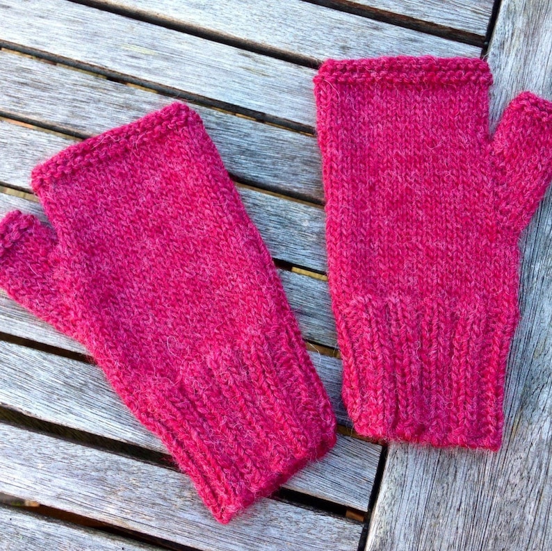 May include: A pair of pink fingerless knitted gloves with a ribbed cuff. The gloves are made of a soft, fuzzy yarn.