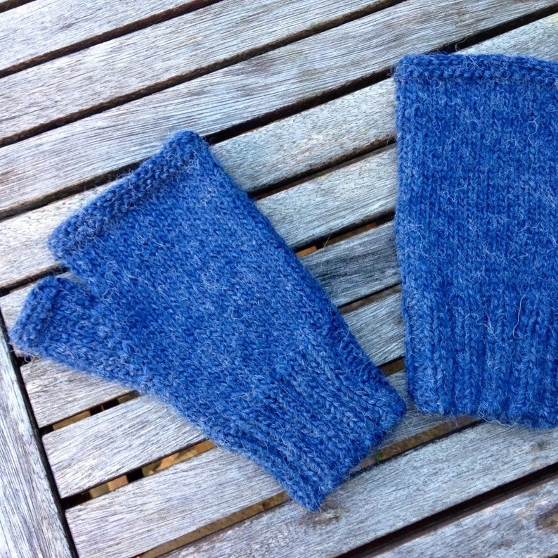 May include: Two blue knitted fingerless gloves on a wooden surface.