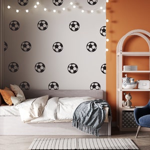 May include: A bedroom with a white bed, a blue armchair, and a white bookshelf with orange shelves. The wall behind the bed is white with black soccer ball decals. The wall behind the bookshelf is orange.
