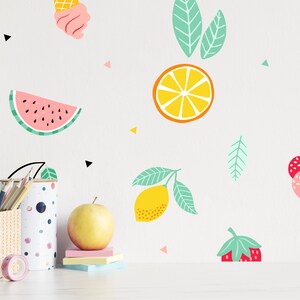 May include: A white wall with colorful fruit and ice cream stickers. The stickers include a watermelon, a lemon, an orange, a pineapple, a strawberry, a cherry, and an ice cream cone. There are also black triangle stickers on the wall.
