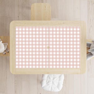 May include: A light wood children's table with a pink and white gingham pattern on the tabletop. The table has a rounded rectangular shape with a small wooden knob in the centre. A small wooden chair is attached to the table.