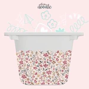 May include: A white storage bin with a floral pattern along the bottom edge. The floral design features pink, brown, and tan flowers with green leaves. The bin has handles and the text "eliza doodle" in the upper left corner.