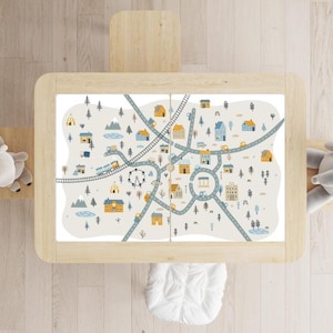May include: A rectangular wooden table featuring a light-coloured tabletop with a printed play mat design. The graphic depicts a town map with roads, a railway track, houses, trees, a Ferris wheel, mountains, and small vehicles in blue, yellow, and grey.