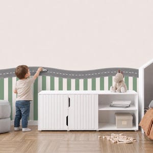 May include: A wall decal featuring a grey road with a white dashed centre line, positioned above a pattern of vertical green and white stripes. The road decal has a wavy top edge and is applied to a wall behind a white storage cabinet.