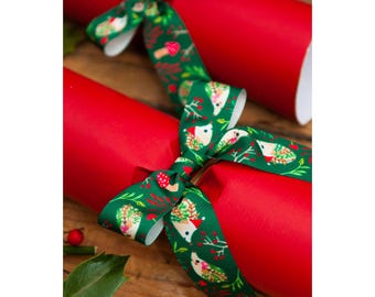 May include: Red Christmas crackers with green ribbon featuring a hedgehog and mushroom pattern. The crackers are arranged on a wooden surface, with a holly leaf and red berries in the foreground. Festive holiday decor.