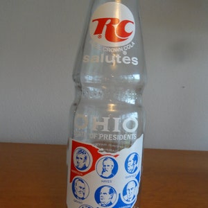 May include: A clear glass bottle of RC Cola with a white label that says "RC Crown Cola salutes Ohio State of Presidents 1776-1976". The label features a map of Ohio with the portraits of eight presidents from Ohio.