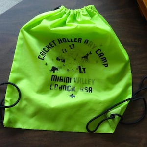 May include: Bright neon green drawstring bag with black drawstrings. The bag features the text "CRICKET HOLLER DAY CAMP" and "MIAMI VALLEY COUNCIL BSA" in black. The bag has a drawstring closure.