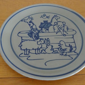 May include: A ceramic plate with a blue and white design featuring animals on an ark. The plate has a blue border and a light gray center. The animals include a giraffe, elephant, and sheep.