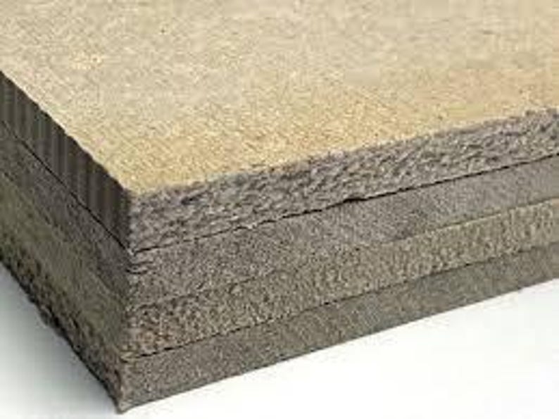 May include: A stack of rectangular, gray-brown composite boards. The boards have a rough, textured surface and appear to be made of layered materials. The edges of the boards show a corrugated pattern.