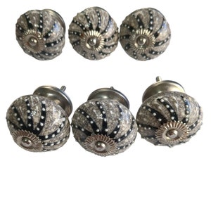 May include: Six ceramic cabinet knobs with a gray and black swirl pattern and silver accents. The knobs are round and have a raised design.