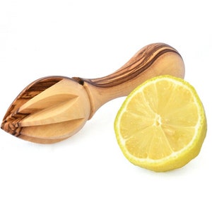May include: A wooden lemon squeezer with a light brown and dark brown wood grain pattern. The squeezer is shaped like a leaf with a handle. A half lemon is next to the squeezer.