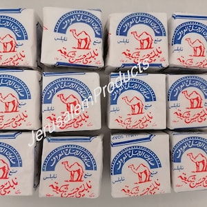 Puede incluir: Doce barras de jabón blanco con letras azules y rojas. El jabón presenta un camello y el texto "صابون الجمل المعروف" que se traduce como "El famoso jabón de camello".
