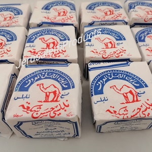 Op de afbeelding: Een stapel witte en blauwe zeepjes met een kameelafbeelding en Arabische tekst. De tekst luidt "صابون الجمل المعروف", wat vertaald wordt als "De beroemde kameelzeep".