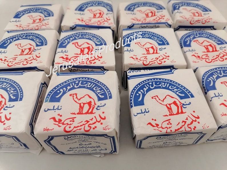 Op de afbeelding: Een stapel witte en blauwe zeepjes met een kameelafbeelding en Arabische tekst. De tekst luidt "صابون الجمل المعروف", wat vertaald wordt als "De beroemde kameelzeep".