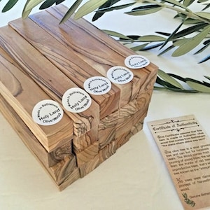 May include: A stack of olive wood blocks with a certificate of authenticity. The blocks are labeled "Holy Land Olive Wood" and "Made in Bethlehem". The certificate explains that the wood comes from olive trees in Bethlehem.
