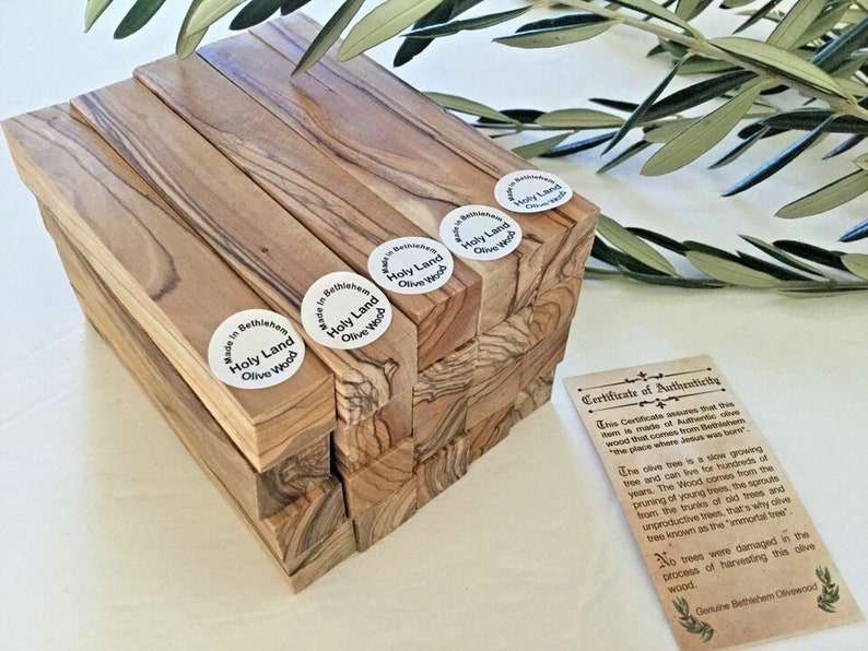 May include: A stack of olive wood blocks with a certificate of authenticity. The blocks are labeled "Holy Land Olive Wood" and "Made in Bethlehem". The certificate explains that the wood comes from olive trees in Bethlehem.