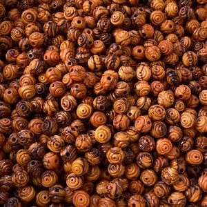 May include: A close-up image of a pile of brown wooden beads with a swirl pattern. The beads are all the same size and shape, and they are arranged in a random pattern.