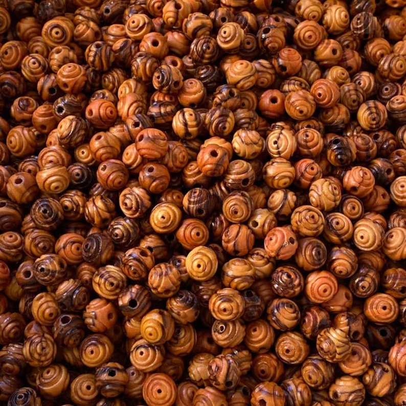 May include: A close-up image of a pile of brown wooden beads with a swirl pattern. The beads are all the same size and shape, and they are arranged in a random pattern.