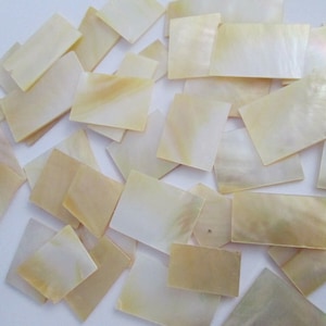 May include: A collection of iridescent, off-white, rectangular mother of pearl shell tiles. The tiles are various sizes and shapes.