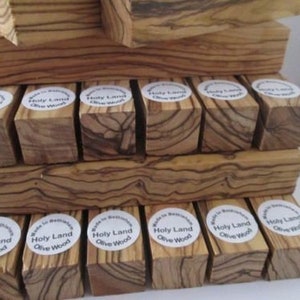 May include: A stack of small wooden blocks made from olive wood. The blocks are all different sizes and shapes, and they have a natural, rustic look. Each block has a label that says "Holy Land Olive Wood".
