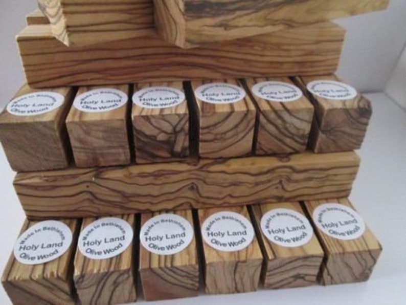 May include: A stack of small wooden blocks made from olive wood. The blocks are all different sizes and shapes, and they have a natural, rustic look. Each block has a label that says "Holy Land Olive Wood".