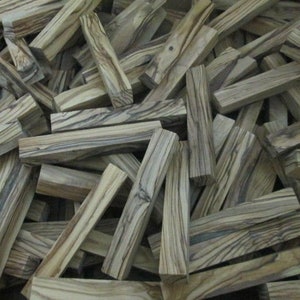 May include: A pile of wooden blanks with a striped pattern in shades of brown and gray. The blanks are all roughly the same size and shape, and they are arranged in a random order.