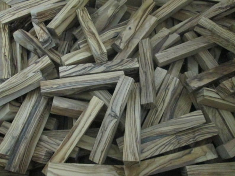 May include: A pile of wooden blanks with a striped pattern in shades of brown and gray. The blanks are all roughly the same size and shape, and they are arranged in a random order.